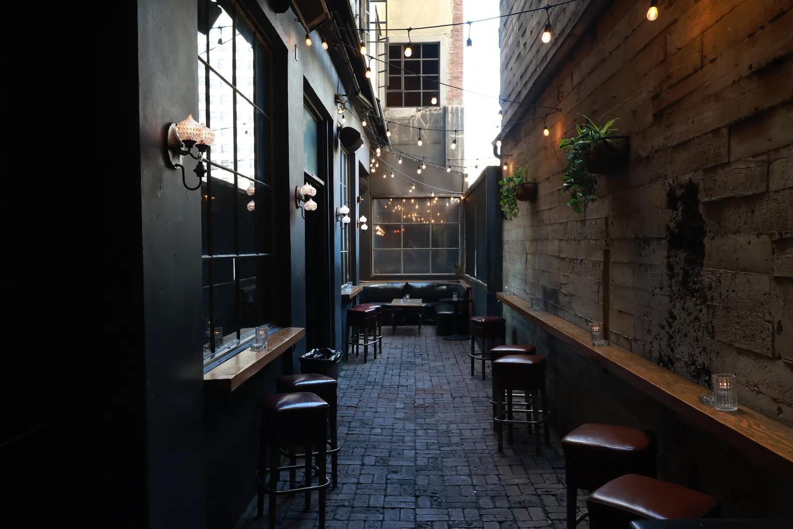 The patio: a brick-paved alley strung with lights, stools along the wall
